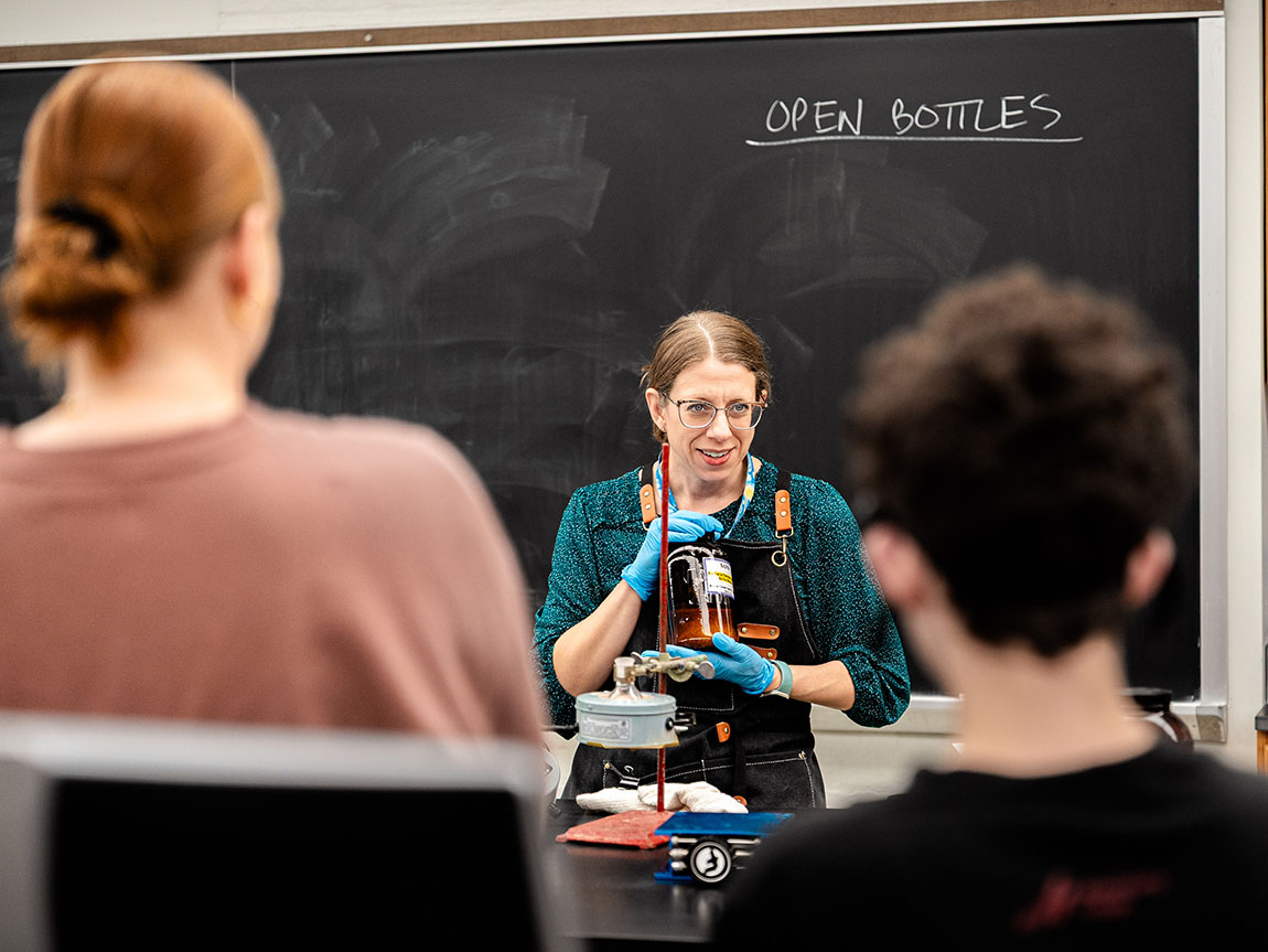 A college chemistry professor holds up a beaker in front of the class